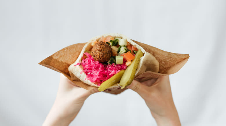 Hands hold a colorful falafel pita