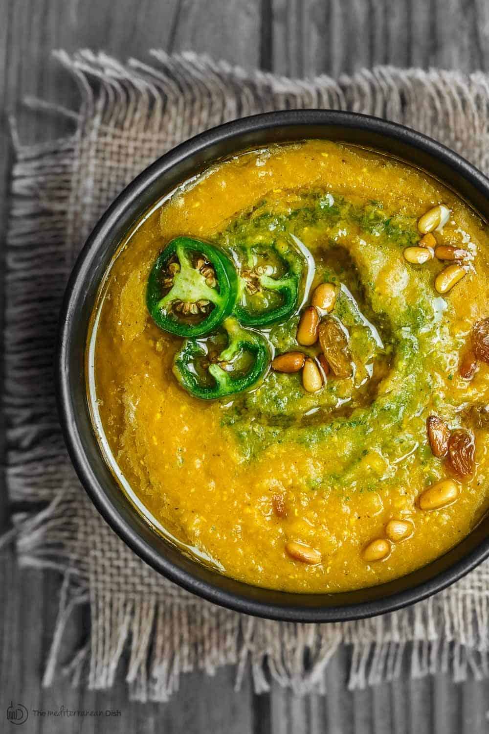 Vegan Pumpkin Soup in serving bowl. Topped with spicy cilantro pesto and jalapenos