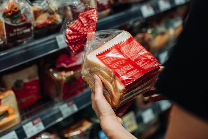 Person holding a loaf of bread from a grocery store shelf